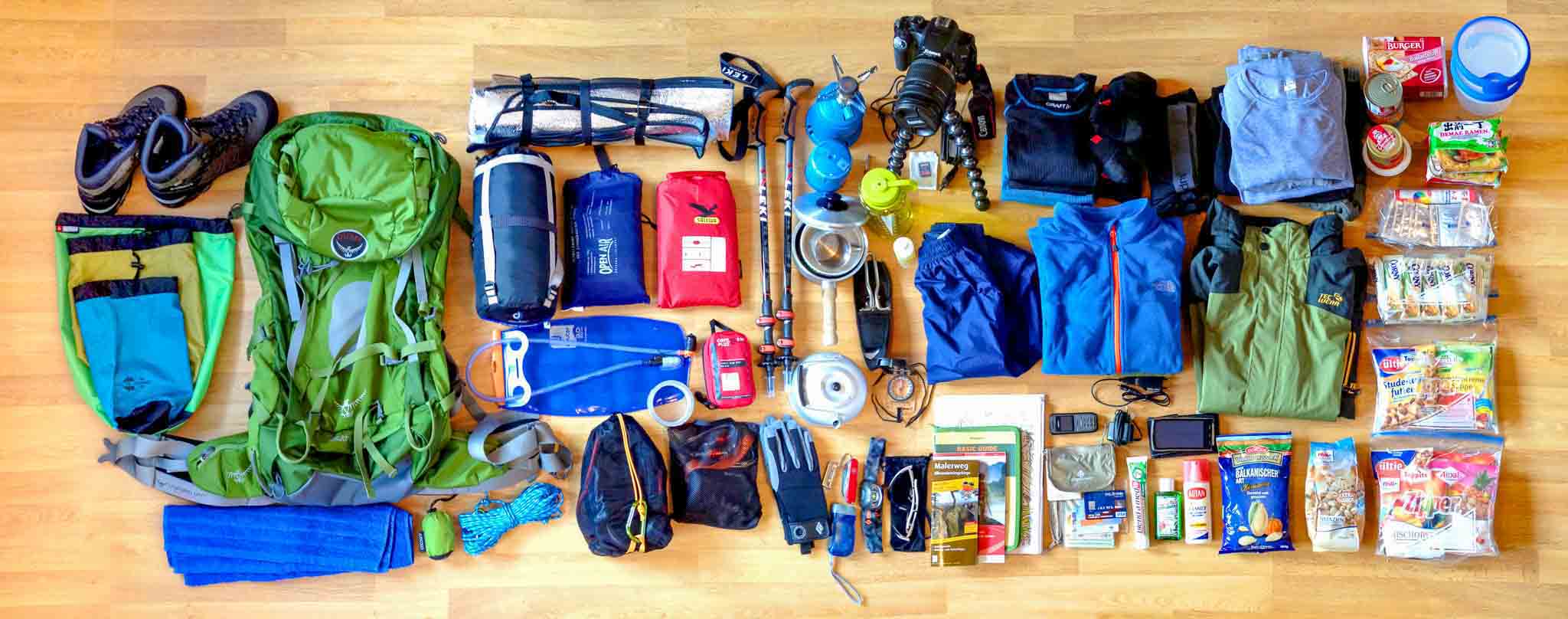 A person is packing for a hiking trip, laying out all the necessary gear and supplies on the floor, including a backpack, tent, sleeping bag, cooking equipment, clothing, food, and navigation tools, to ensure they have everything they need for a safe and enjoyable adventure.